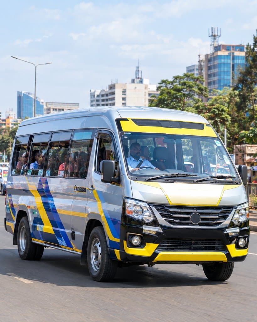 A passenger minibus in yellow and blue livery driving down a busy city avenue.
